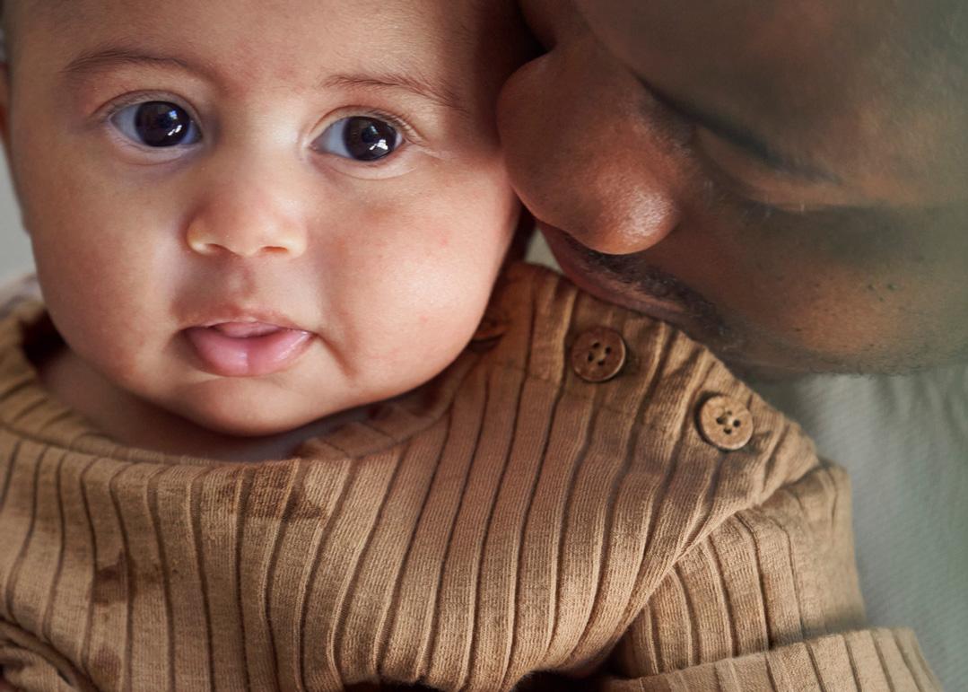A close-up of a baby in a brown sweater being gently snuggled by an adult, creating a warm, tender moment.