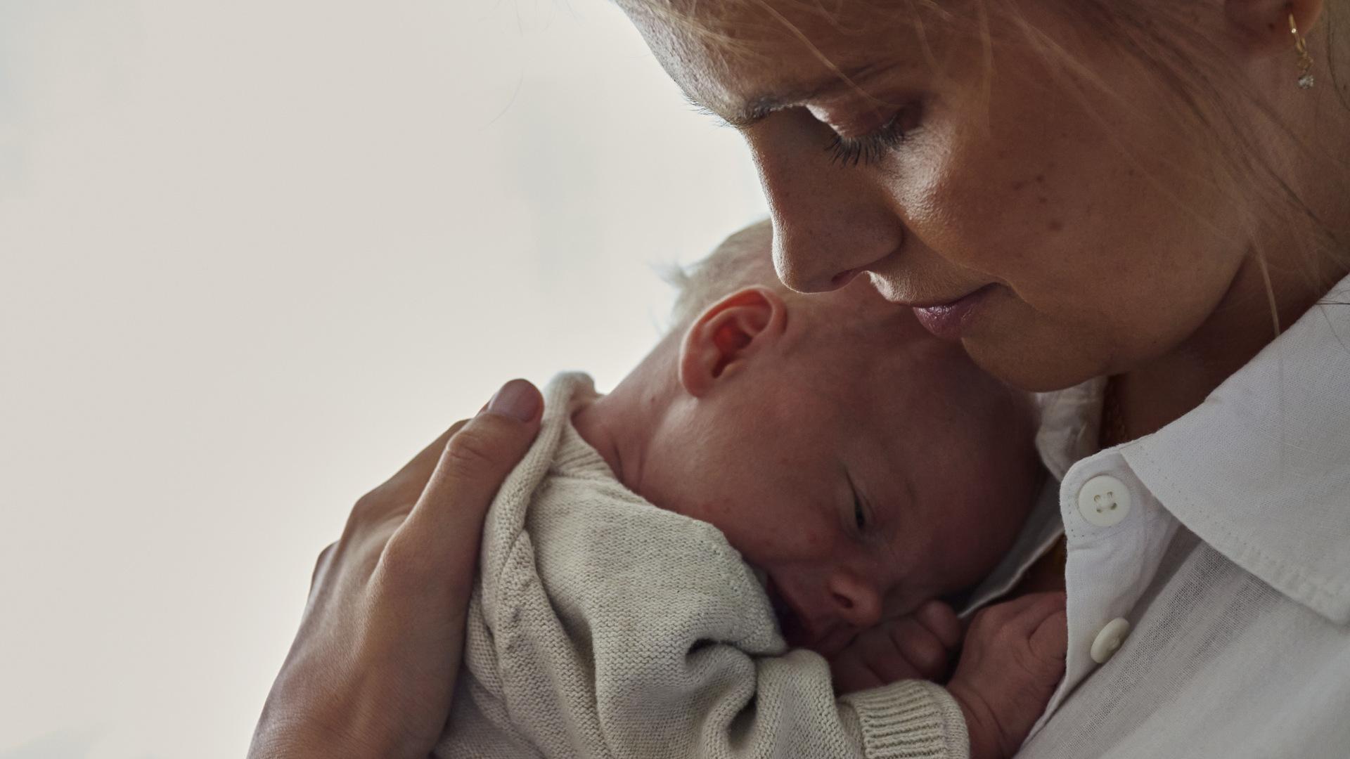 A woman gently cradles a sleeping baby close to her chest, both wearing soft, cozy clothing.